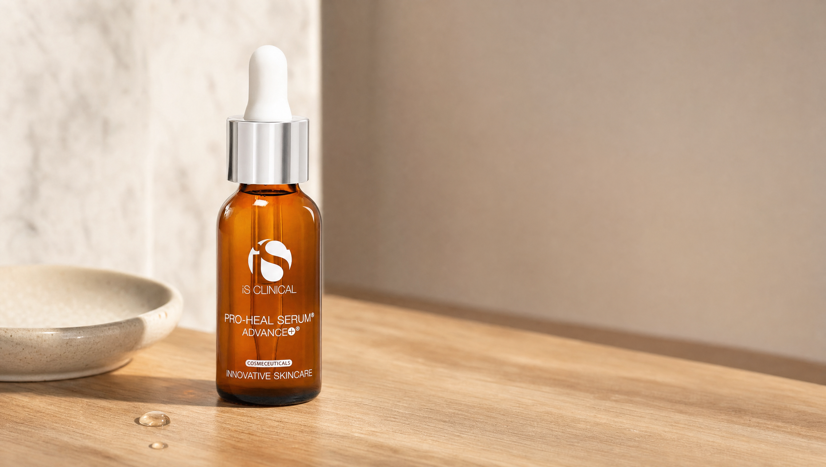 iS Clinical Pro-Heal Serum Advance+ dropper bottle on a honey-oak surface with a ceramic dish