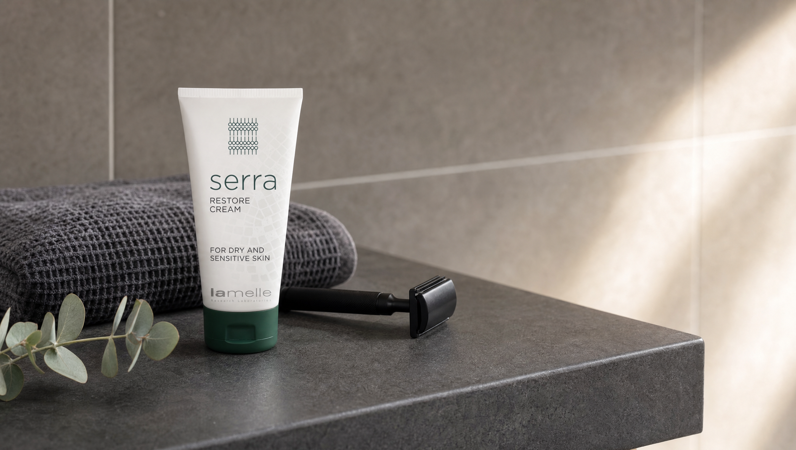 Lamelle Serra Restore Cream tube with a razor and folded towel on a dark stone bathroom shelf in morning light