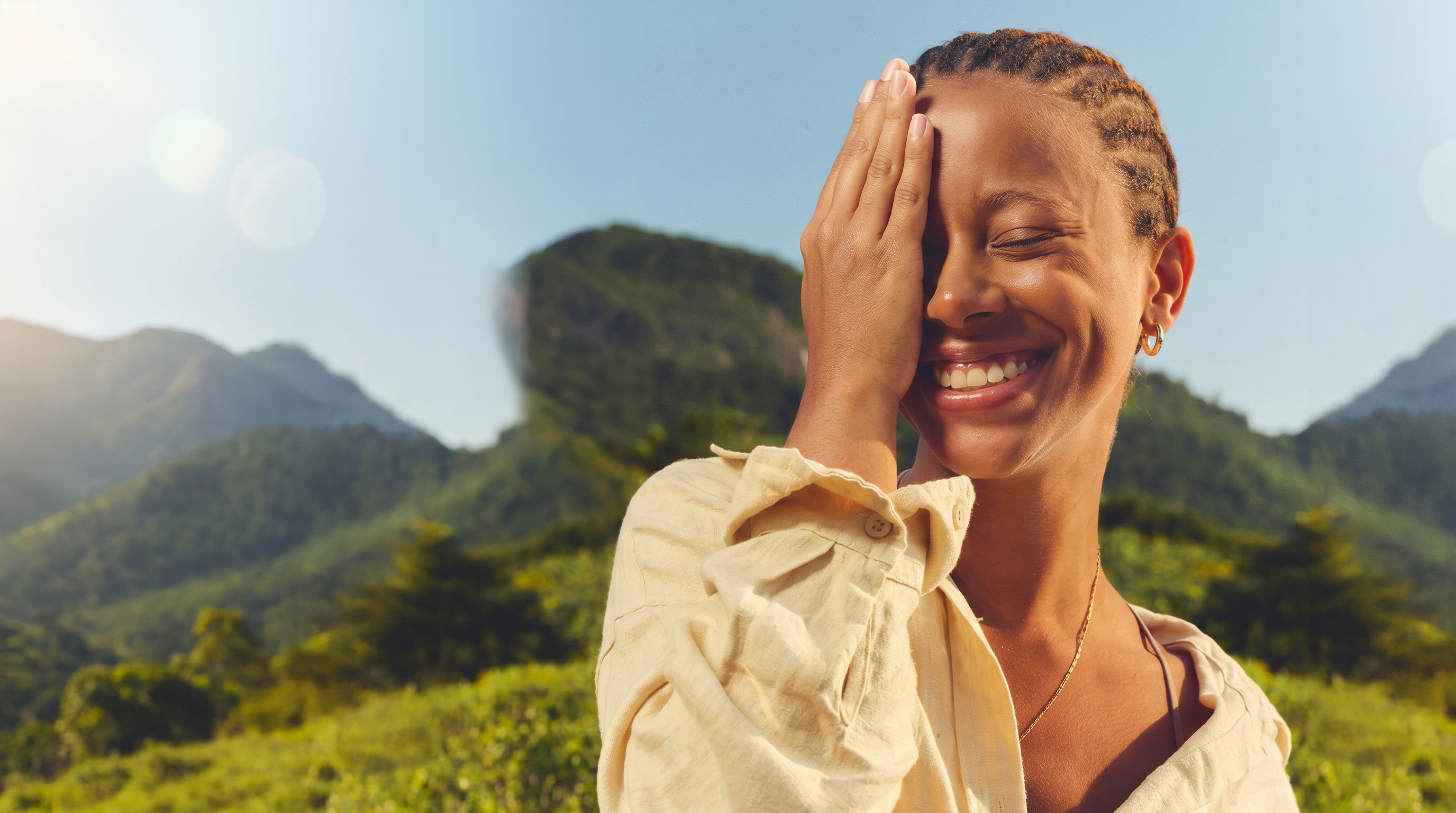 A joyful woman laughing in warm sunlight against lush green mountains.