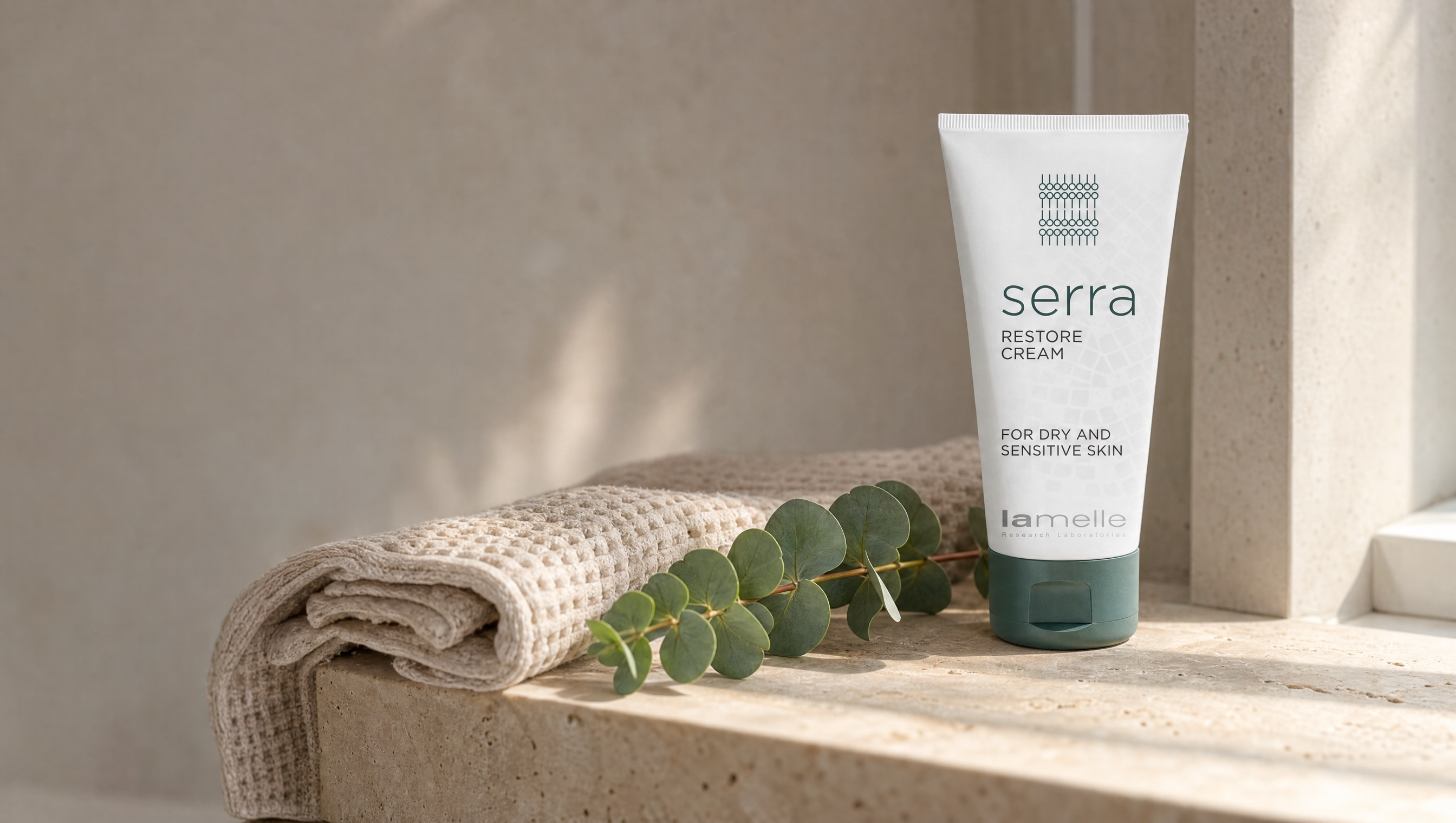 Lamelle Serra Restore Cream tube on a warm travertine ledge with a linen towel and eucalyptus sprig